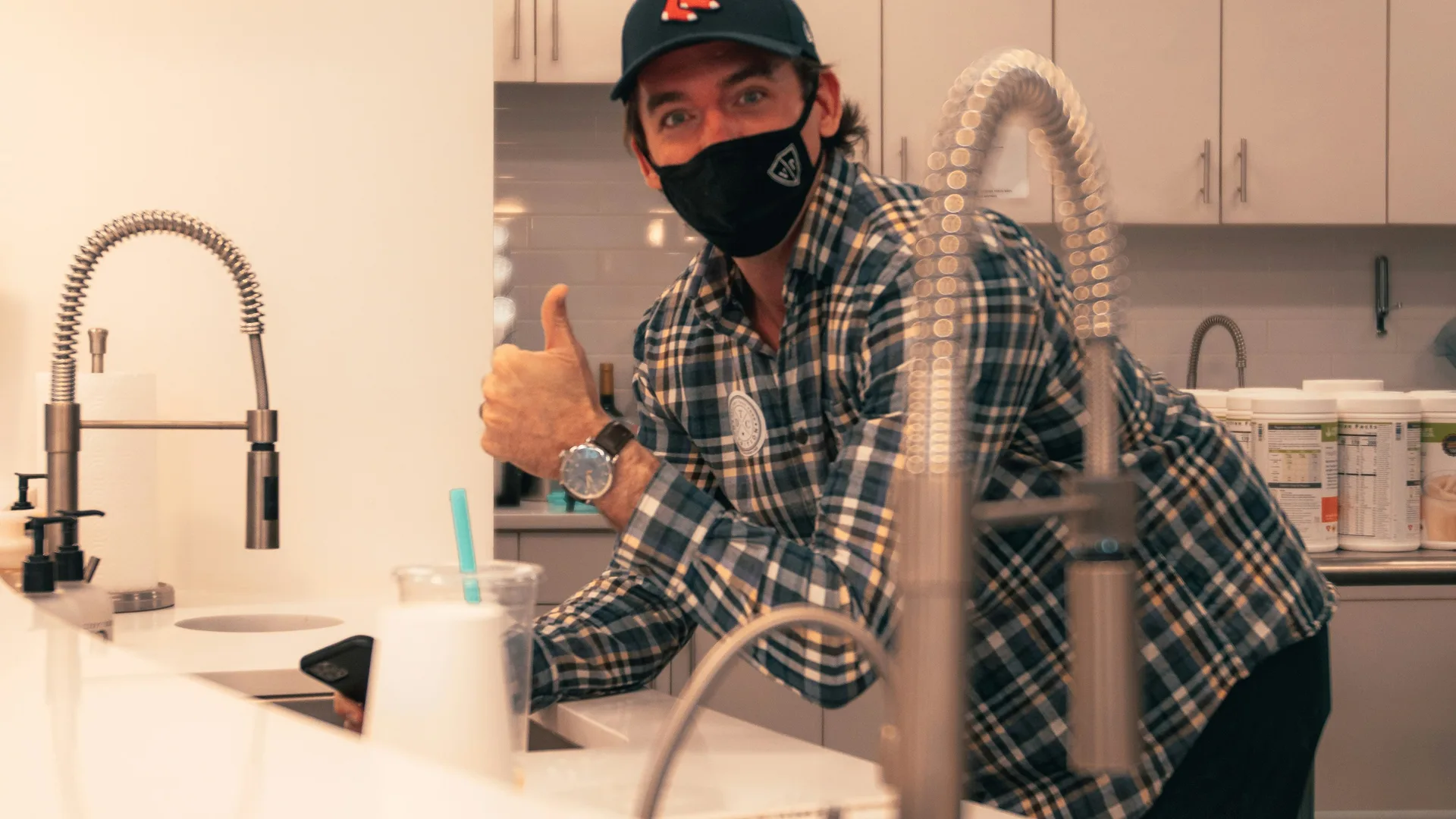 A plumber in a face covering working at a kitchen tap fitting